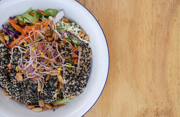Healthy food. Top view of a salad with carrot, lettuce, peanuts, chicken breast breaded with seeds, soy sprouts and cabbage, in a white bowl on the wooden table.
