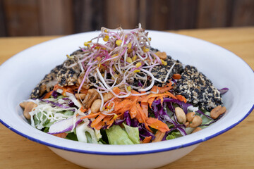 Healthy food. Top view of a salad with carrot, lettuce, peanuts, chicken breast breaded with seeds, soy sprouts and cabbage, in a white bowl on the wooden table.