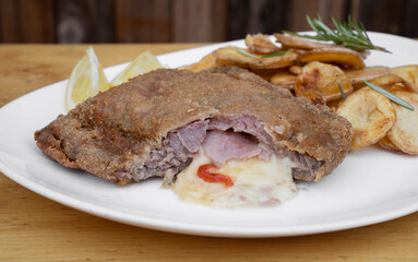 Sliced milanesa, breaded fried steak, stuffed with mozzarella cheese, ham and bell pepper with Spanish chips and lemon, in a white dish.