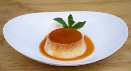 Traditional gourmet dessert. Closeup view of a flan with cream and caramel, in a white dish on the wooden table. 