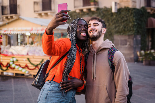 Couple enjoying a road trip in the city center. Interracial couple pose for a selfie holding each other with evening sun in the background.