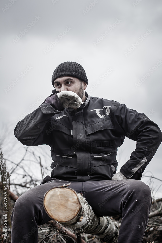 Wall mural the man was tired of sawing fallen trees and sat down on a log to rest. a caucasian man is in charge