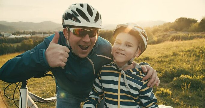 Father teaching son to ride bicycle. Happy cute boy in helmet learn to riding a bike in park on green meadow in summer day at sunset time. Family weekend. 4K video Slow motion
