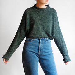 Woman wearing oversized green sweater and blue mom jeans isolated on white background	