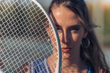 Closeup shot of a young attractive caucasian female posing with a tennis racket on a court