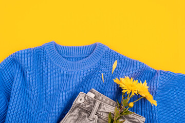 Yellow chrysanthemums on a blue sweater and gray jeans on yellow background. Women's Day, March 8, birthday, valentine's day concept. Wool sweater with flowers. Top view, flat lay