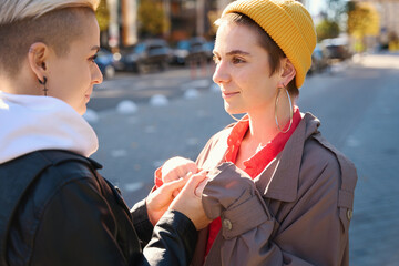 Young women stand against backdrop of the city landscape, hold hands