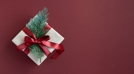 Banner with craft gift box with thuja and red ribbon on a red background. Top view, copyspace.