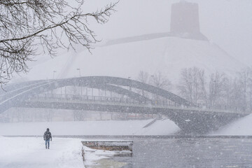 a person walking near a river during heavy snowfall - obrazy, fototapety, plakaty