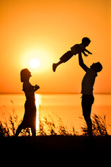 Silhouettes of Happy family, mother and father holding son on backdrop of setting sun. Father's Day background on Orange sunset at sea.