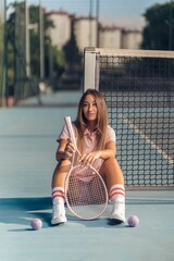 Vertical shot of a young female in pink athleisure posing with a pink racket on a tennis court