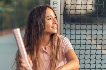 Attractive young caucasian female in pink athleisure posing with a pink racket on a tennis court