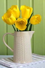 bouquet of yellow tulips in a jug on a green background.