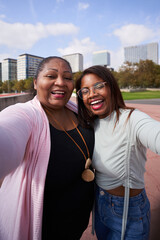 Cheerful Latin American mother and adult daughter, taking a selfie cheerfully. City background.