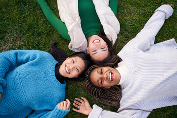 Joyful portrait of three best friends lying on grass having good time laughing and looking at camera
