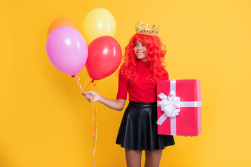 happy kid in crown with present box and party balloon on yellow background