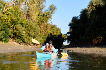 Fototapeta na wymiar Rear view of woman kayaking on blue kayak in river at autumn