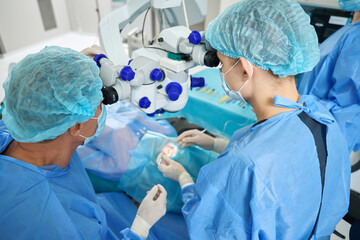 Medical worker and assistant doing laser vision correction operation