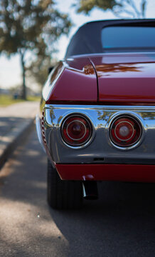 rear of red classic muscle car parked on the street during the daytime showing taillight chrome bumper tailpipe