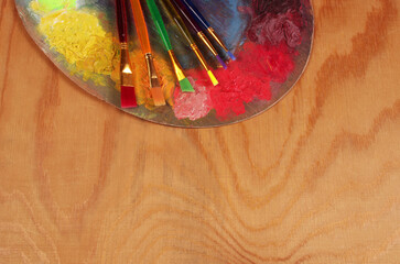 Artistic palette, paints and brushes on a wooden texture background.