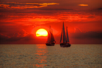 Sea background with two sailing ships. Reflection of the sun on the waves. Soft red sunlight.