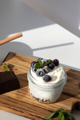 Yogurt in a glass jar with granola, chocolate, blueberries and honey on a wooden board on a white background with mint leaves. Top view
