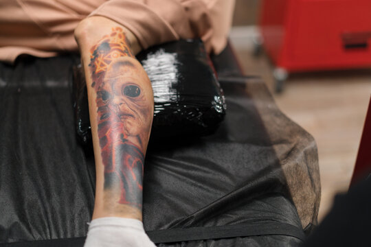 Tattoo with an alien on the leg of a woman during a tattoo correction session in a tattoo studio