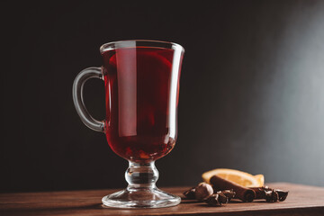 Mulled red wine in a glass and spices on wooden board, dark background