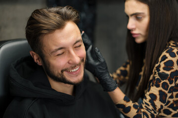 Tattoo piercing studio - a woman makes an ear piercing to a man to a guy