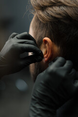 Tattoo piercing studio - a woman makes an ear piercing to a man to a guy