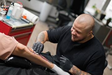 Close-up - the process of tattooing a woman on her leg. Male tattoo artist making a tattoo