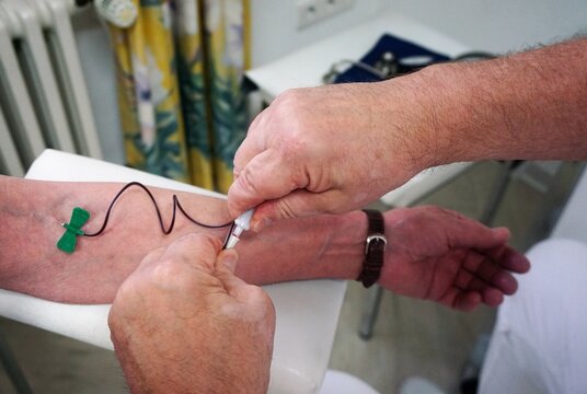 Hände von Arzt legen Kanüle zum Blut abnehmen aus Arm von Patientin in Arztpraxis 