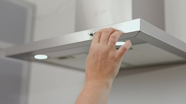 a woman's hand presses the buttons on the kitchen hood. Pushing a button. Turning on the range hood cooking ventilation over an oven