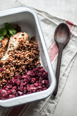 Baked chicken legs on a baking sheet with boiled buckwheat and wooden spoon.