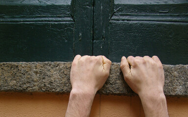 two hands clinging to a window sill, concept of risk or strength
