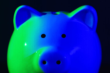 Close up Piggy bank on a dark background with green-blue backlight. Banking concept. Bright neon lights