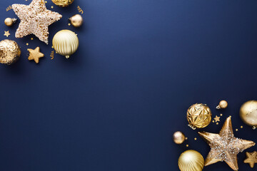 Gold Christmas decorations on dark blue background. Frame of sparkle Xmas stars and baubles. Flat...