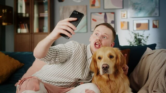 British redhead man together with dog retriever making selfie photo or video call on front camera smartphone. Positive young student man conference call with pet for blog.