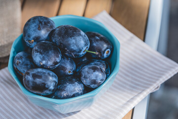 Fruit background, organic fruits. Still life food. Ceramic bowl full of raw fresh blue plums on a rose striped kitchen cloth and rustic wooden table. 