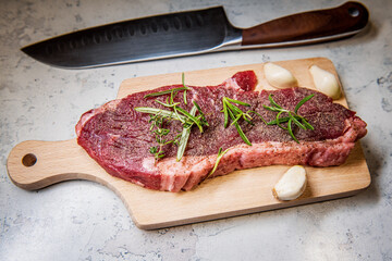 Seasoned raw sirloin beef steak on cutting board with thyme rosemary and garlic