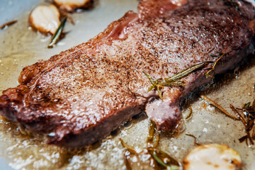 Seasoned sirloin steak grilled on pan with butter, thyme, rosemary and garlic