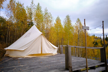 Glamping. A large tent is arranged on a wooden pedestal among autumn trees in the mountains. A place to relax in nature