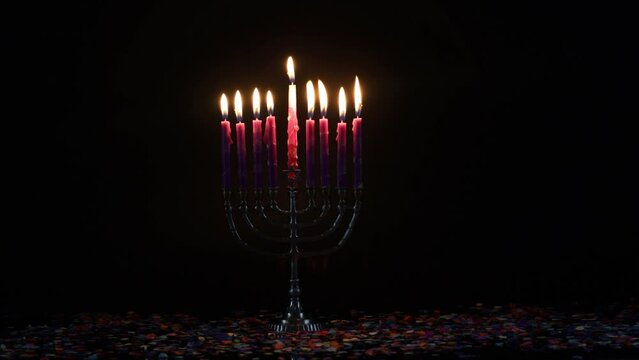 Hanukkah candles on menorah burning in dark room.