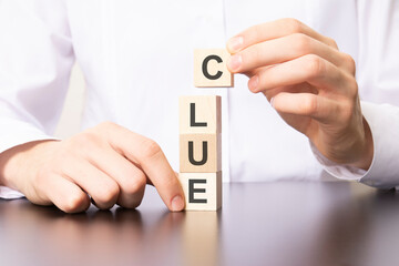 wooden cubes with the word CLUE, the hand puts a cube with letter C.