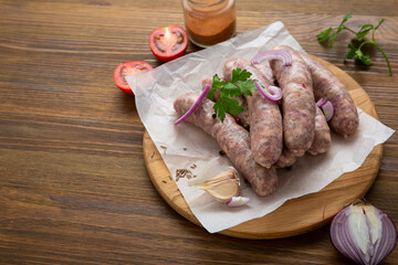 Close up of uncooked bbq sausage on wooden board with spice onion tomato