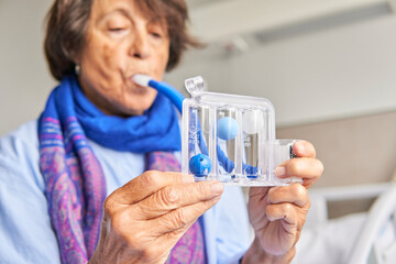 spirometer for breathing exercises. senior woman in hospital room practicing with spirometer