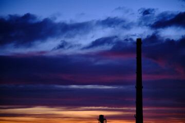 Silhouette of a factory with a large industrial pipe, against the background of an incredible sunset or sunrise sky