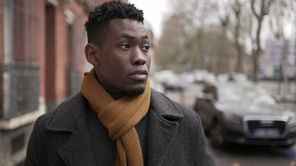 Elegant young black man walking in sidewalk during winter season exploring city or commuting