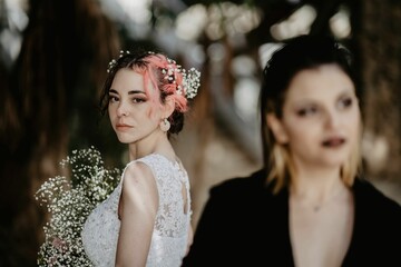 Closeup of two females, one with a brides dress and bouquet and another with black suit and lipstick