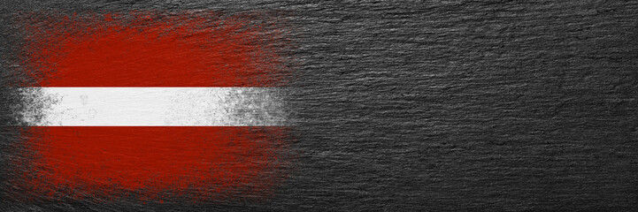 Flag of Latvia. Flag is painted on black slate stone. Stone background. Copy space. Textured background